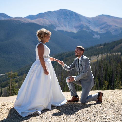 Groom on one knee with mountains in background